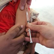 Criança recebe uma dose de vacina aplicada por profissional de saúde em uma unidade clínica.