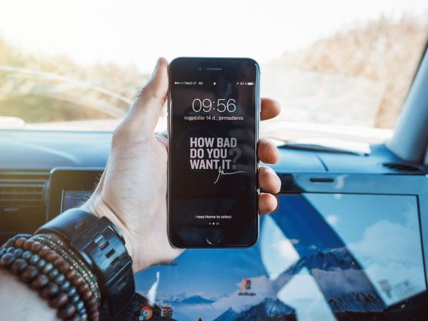 Mão segurando um celular dentro de um carro, representando a consulta digital de serviços de trânsito.