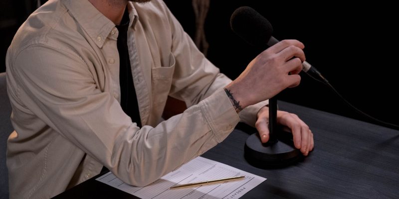 Profissional prepara um podcast em estúdio, diante de um microfone e anotações.
